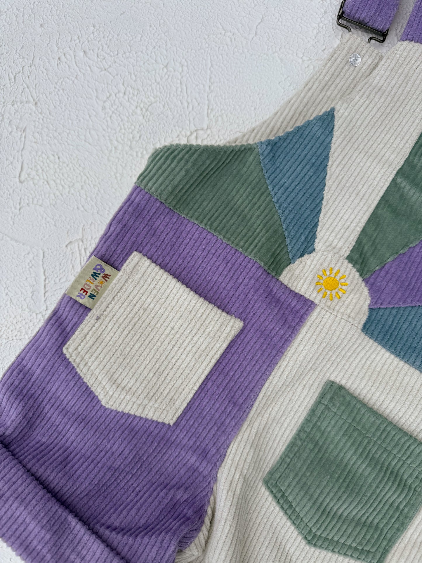 Color-blocked overalls with purple, green, and beige sections on a textured white background