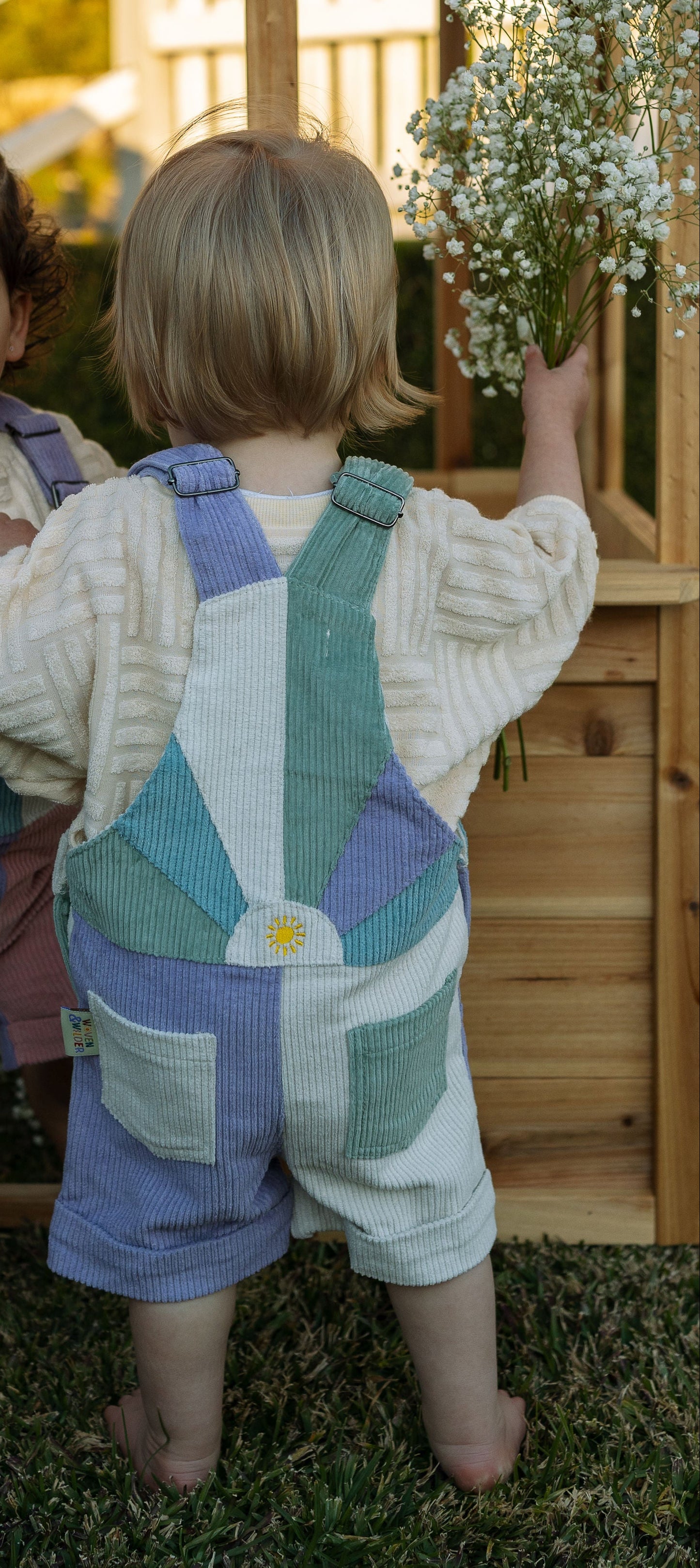 Two children wearing matching outfits with suspenders outdoors.