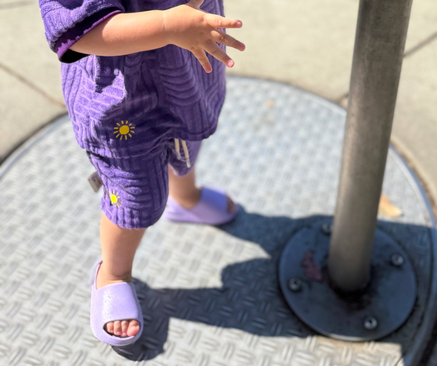 Child wearing purple outfit with sun design and matching shoes, standing on a textured surface.