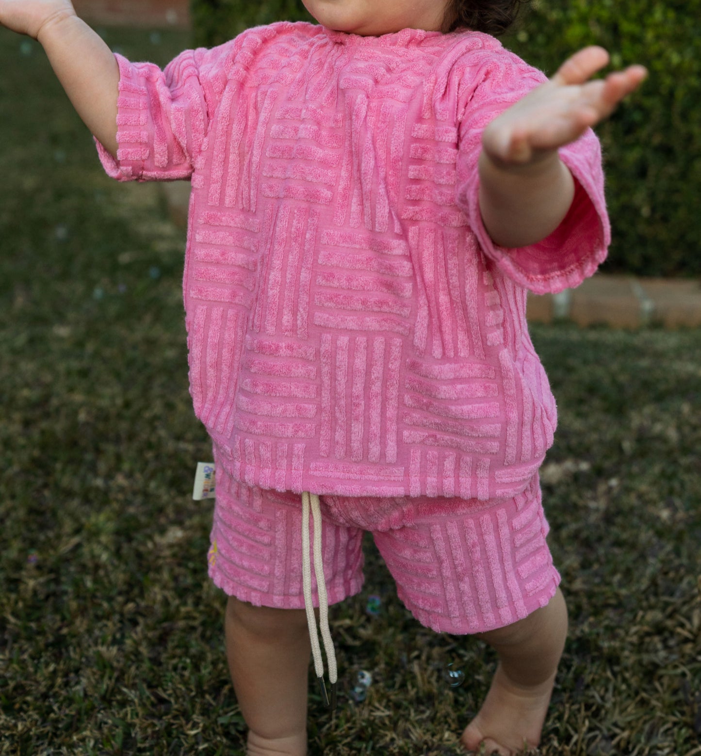Child wearing a pink textured tshirt with a tag outdoors on grass