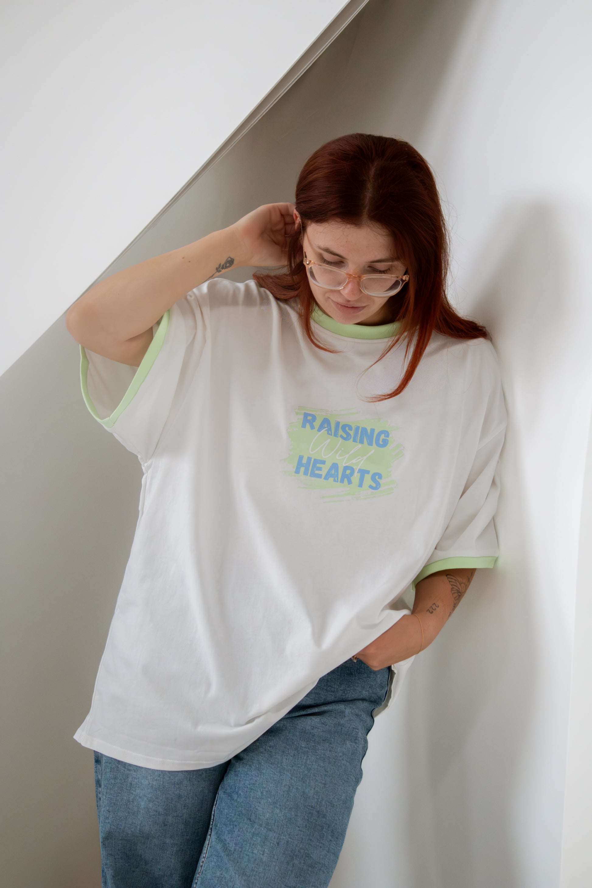 Person wearing a white oversized t-shirt with text, standing against a plain wall.