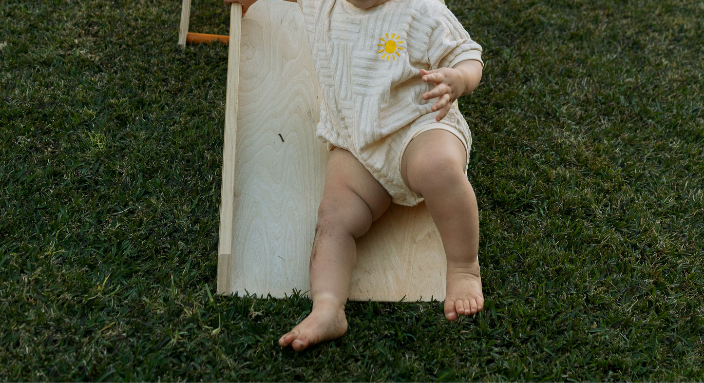 Baby wearing an overall sitting on a slide in grass