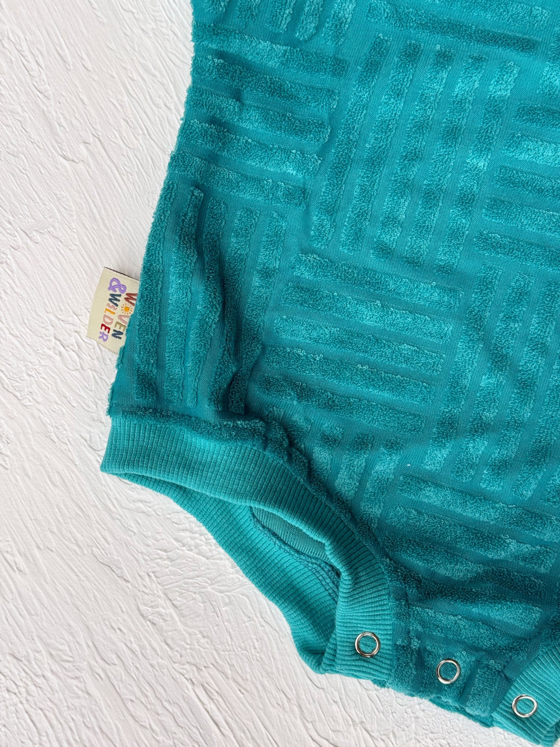 Teal baby romper with a tag on a white background