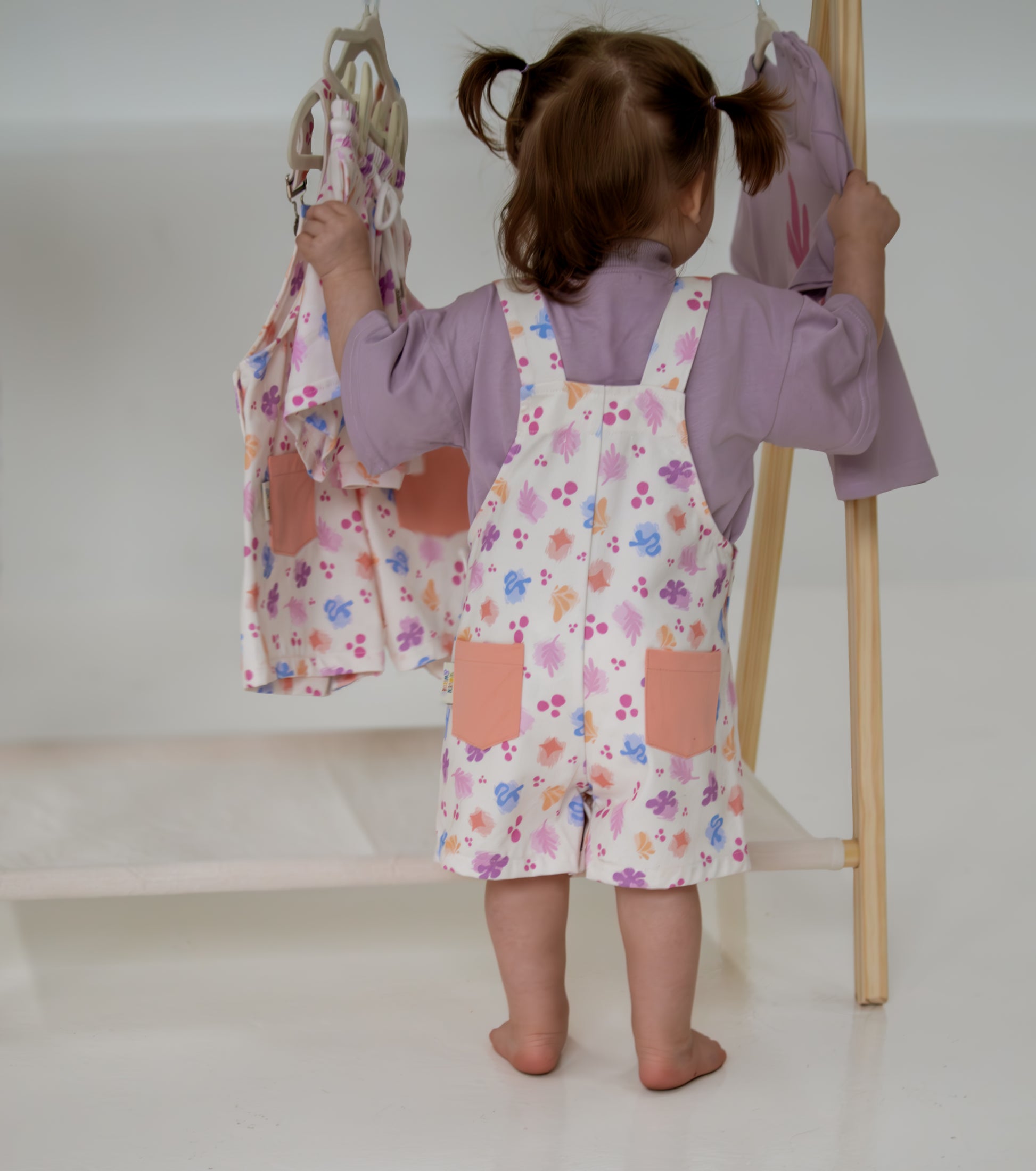 Child wearing a floral dress with pink pockets, standing in front of a mirror.