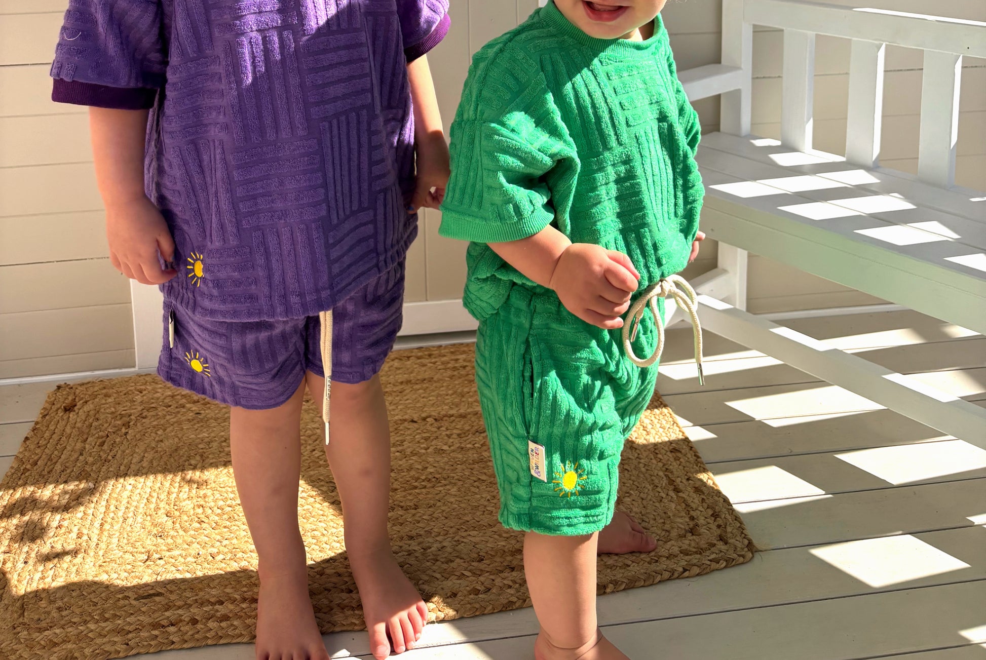 Two children wearing romper on a wooden deck.