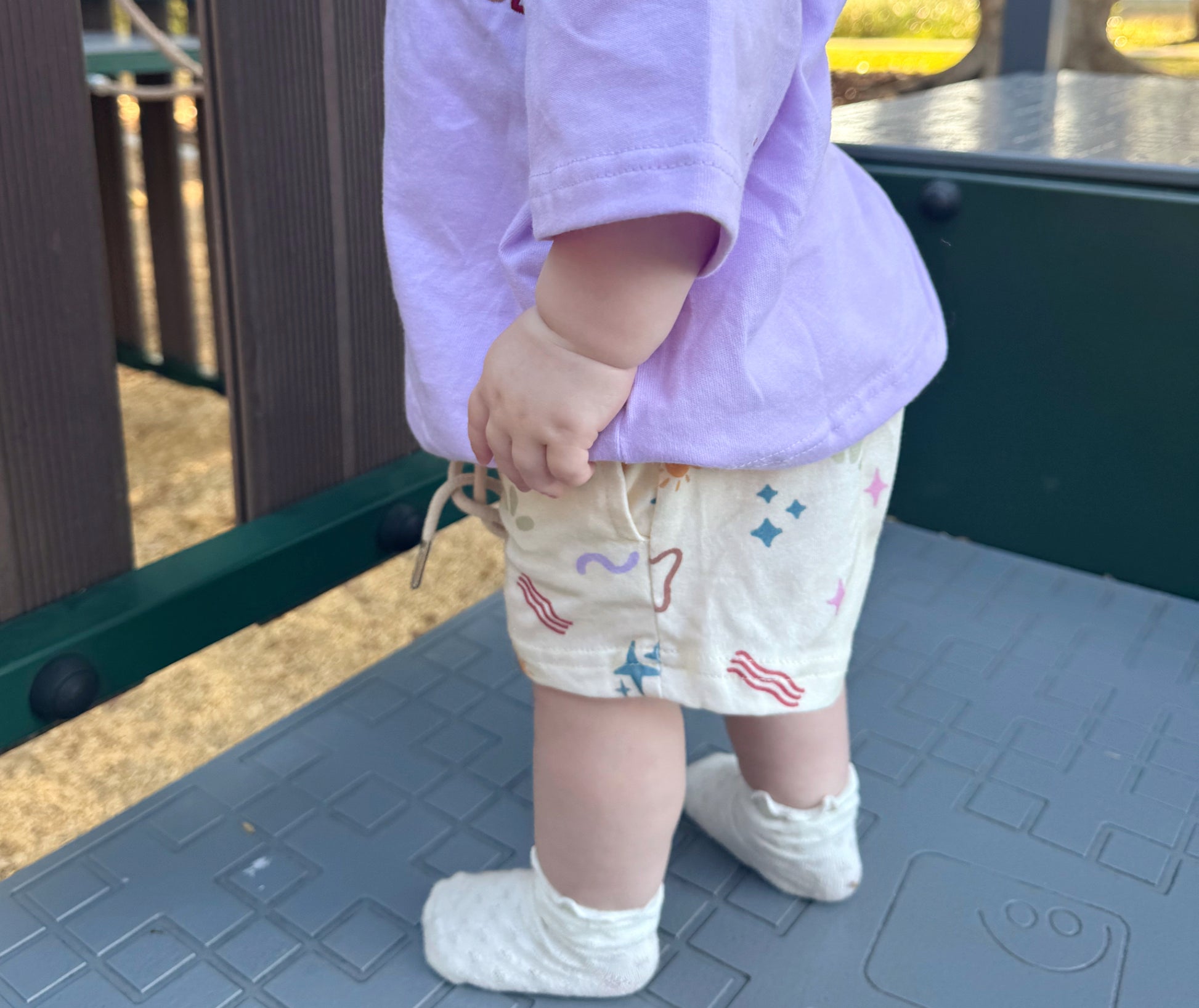 Child wearing a purple shirt and patterned shorts on a playground surface