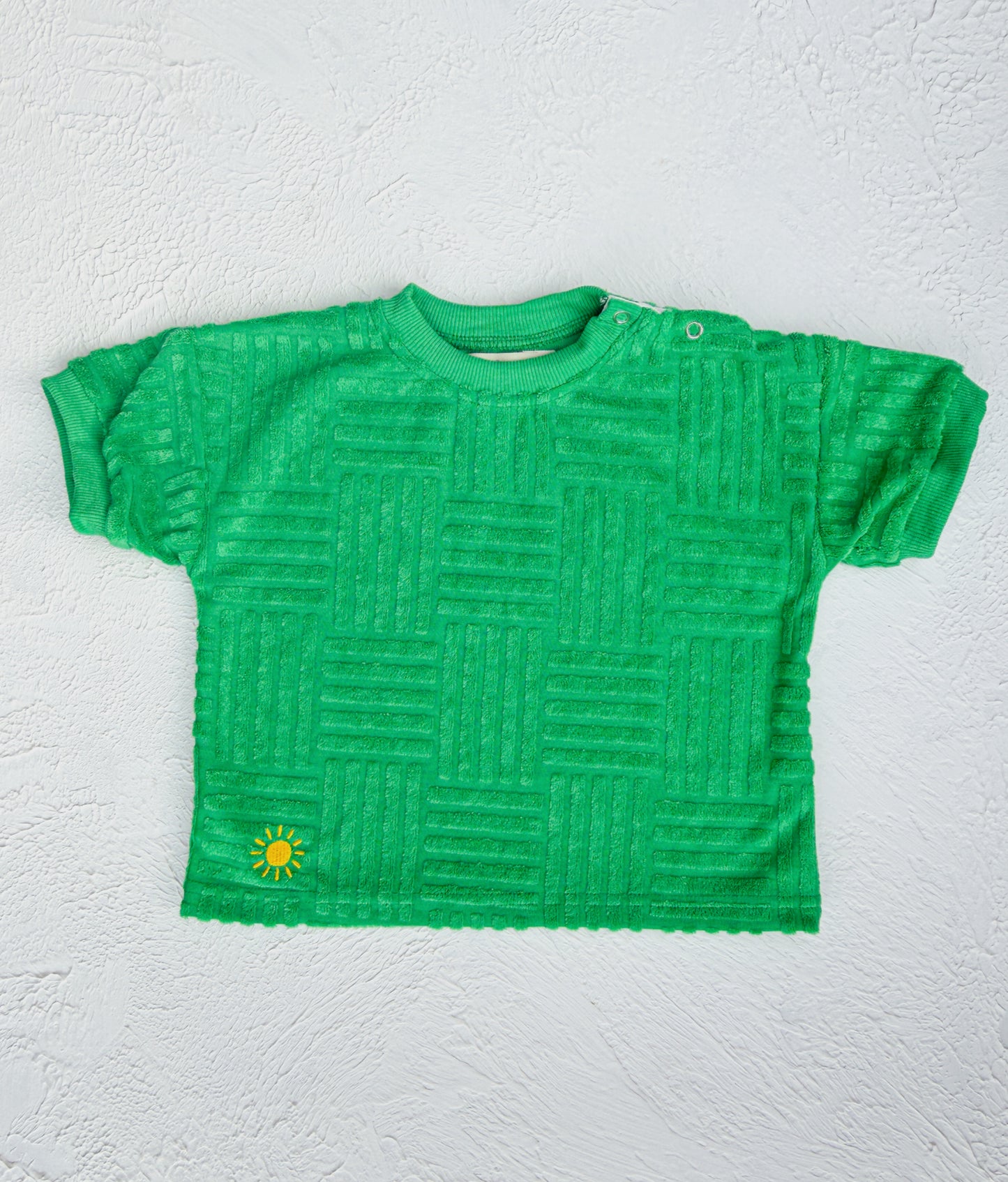 Green textured t-shirt with a small yellow logo on a white background