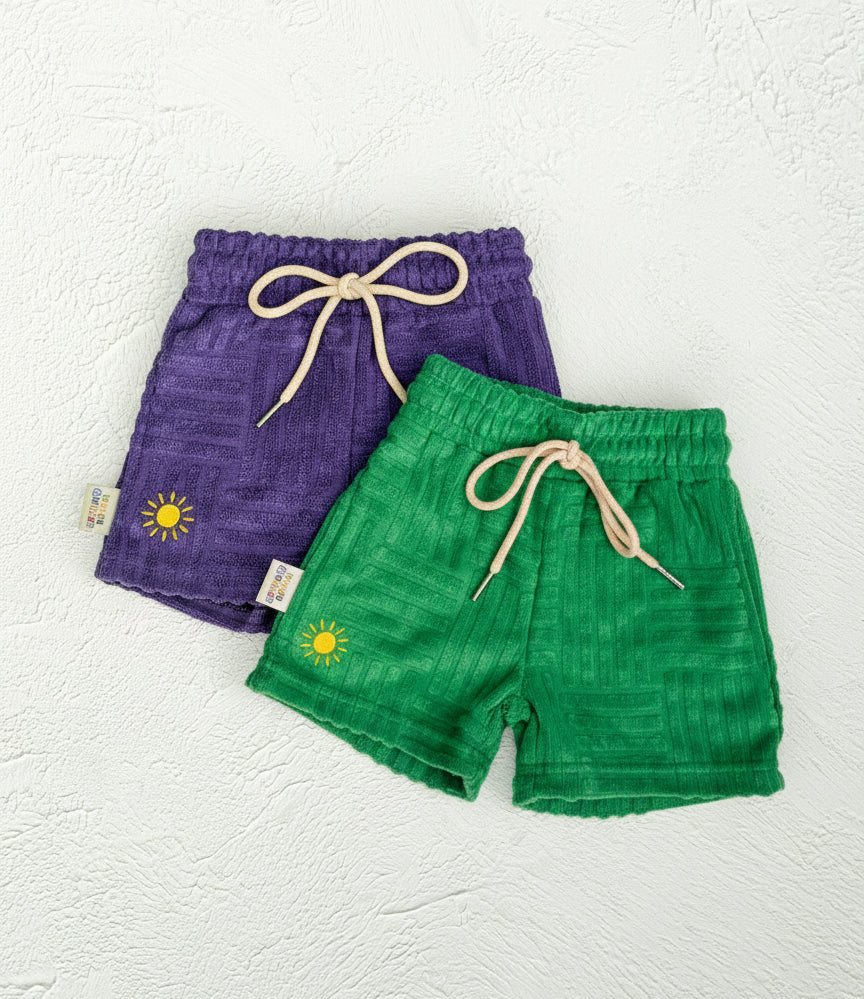 Purple and green shorts with sun design on a textured white background