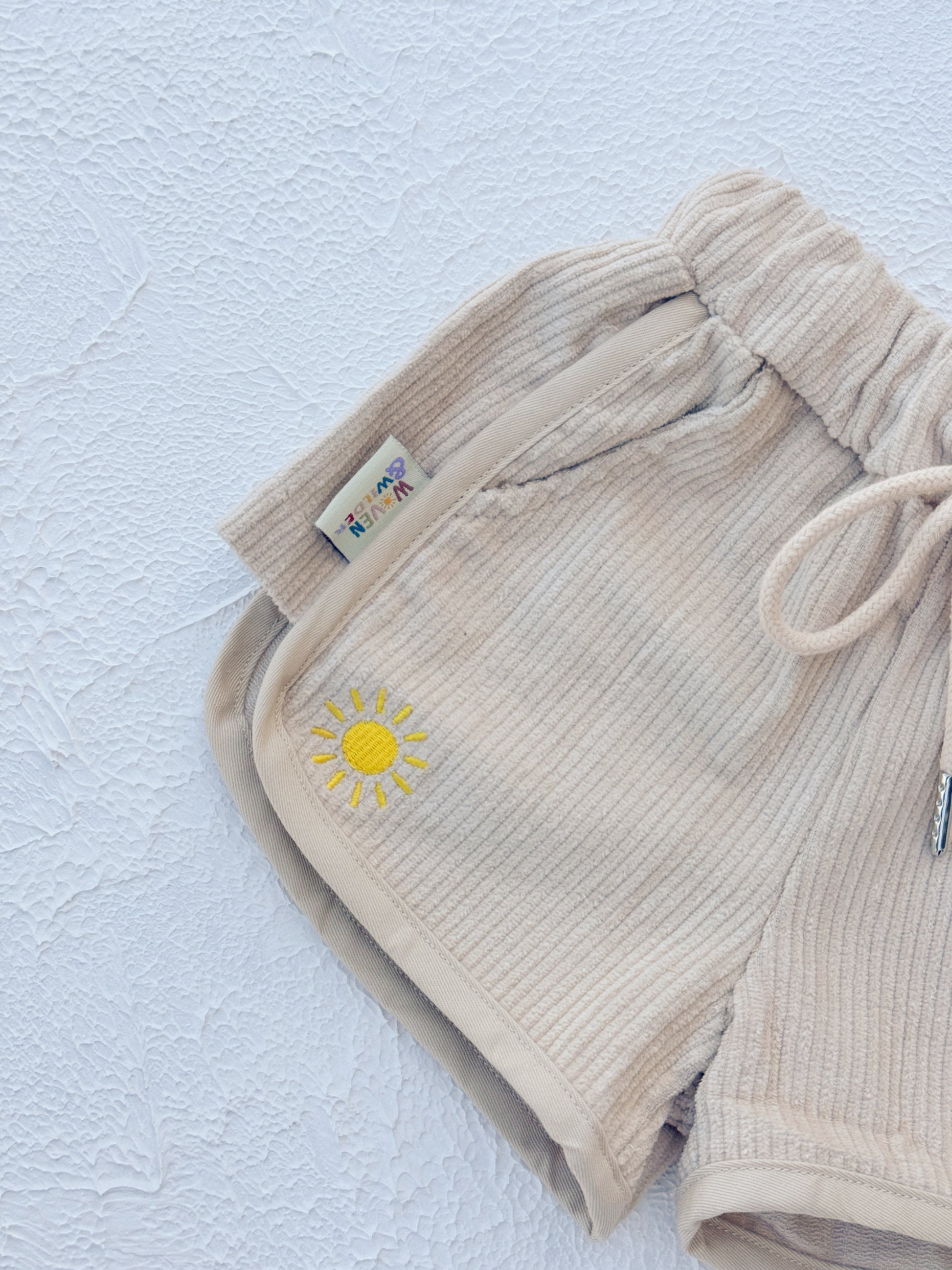 Beige shorts with a sun emblem on a light blue textured background