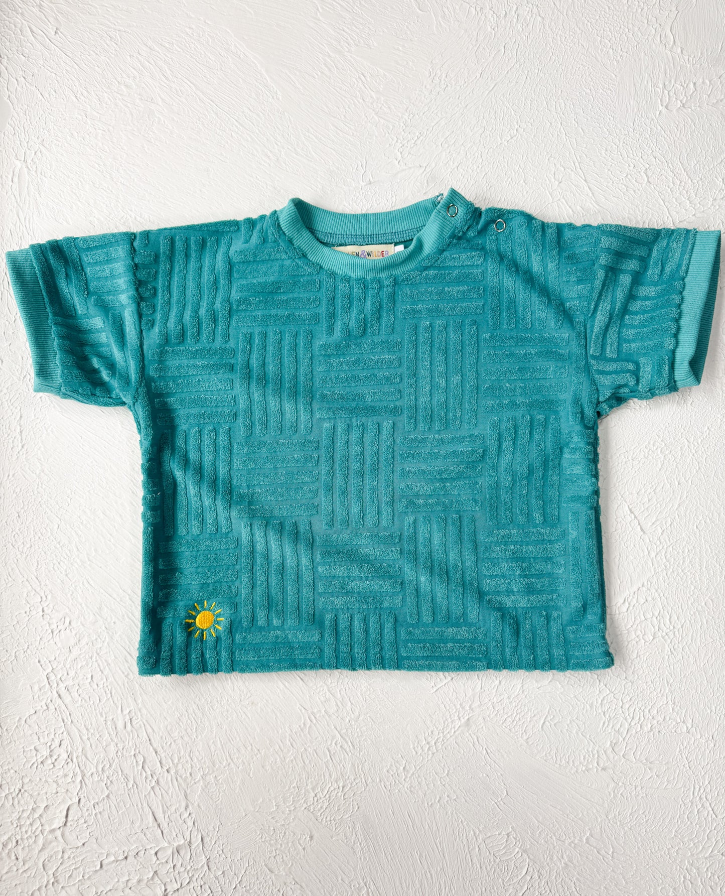 Teal textured t-shirt with a small yellow flower design on a white background