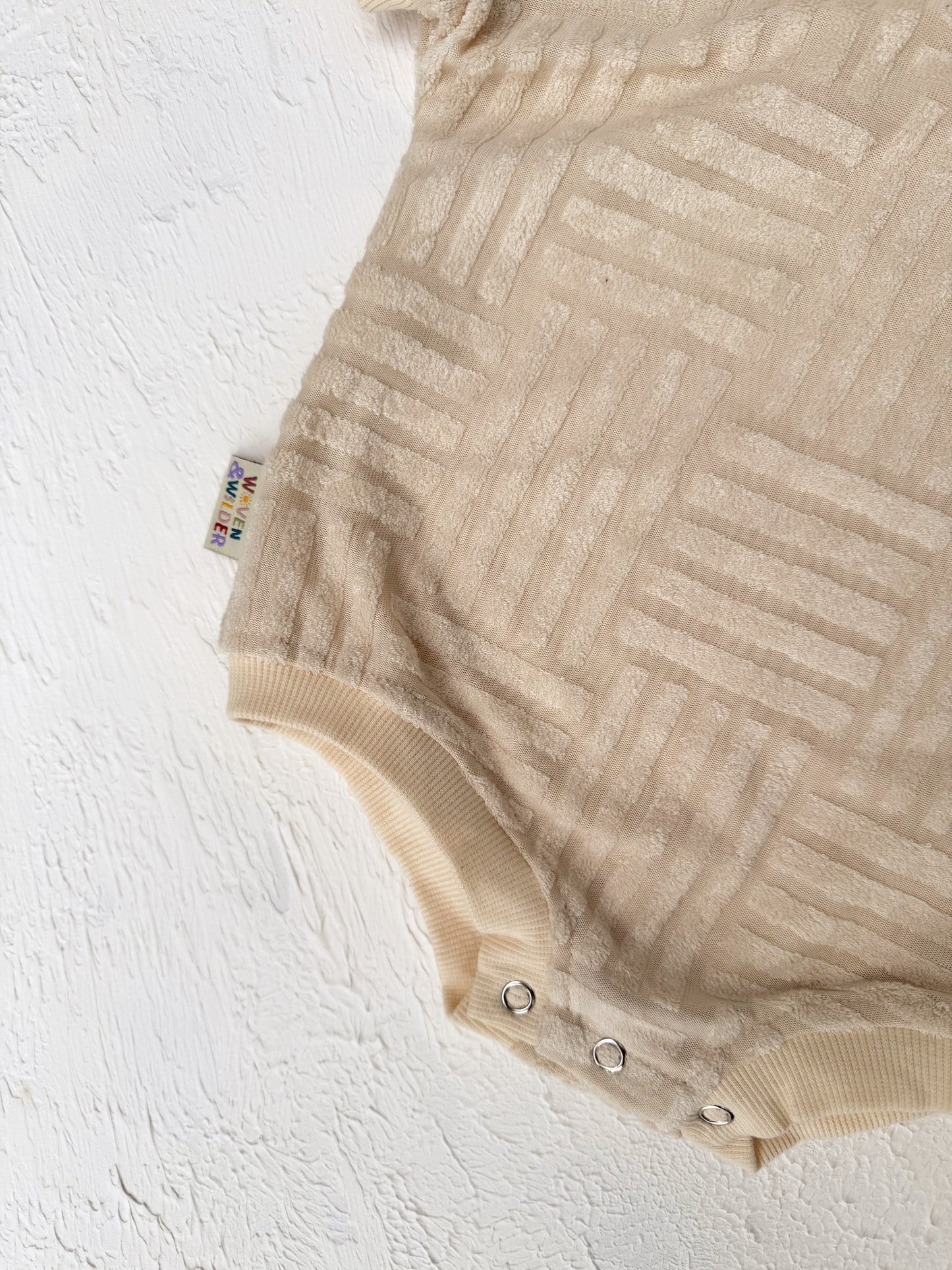 Beige baby romper with a textured pattern on a white background