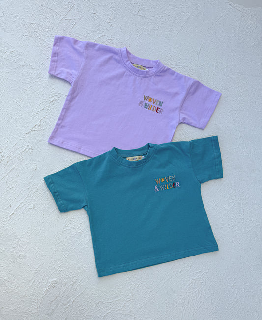 Two t-shirts, one purple and one blue, with 'Woven & Wider' text on a light gray background.