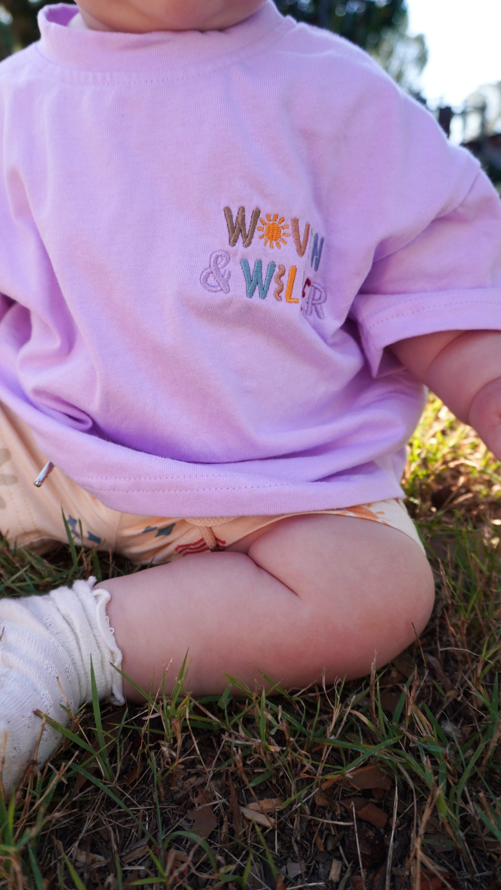 Child wearing a pink sweatshirt with colorful text sitting on grass