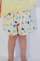 Child wearing a yellow shirt with a green graphic and patterned shorts on a white background