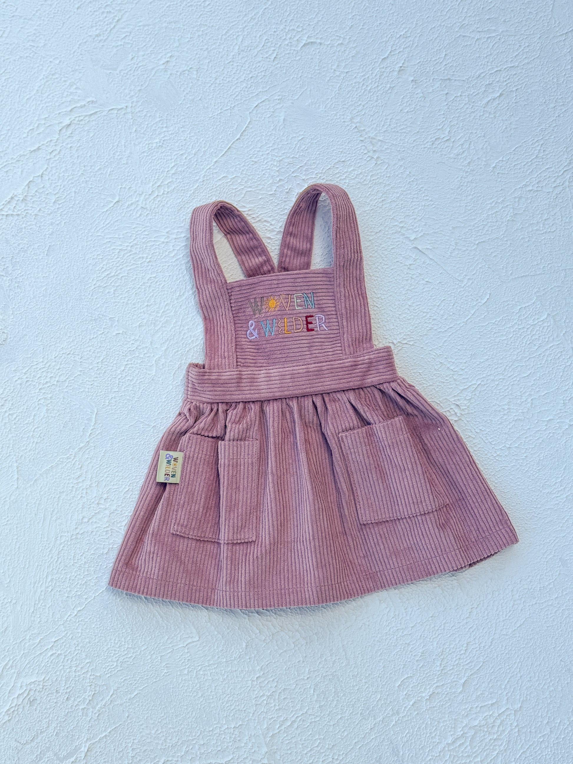 Pink striped dress with 'Woven & Wilder' text on a light blue background