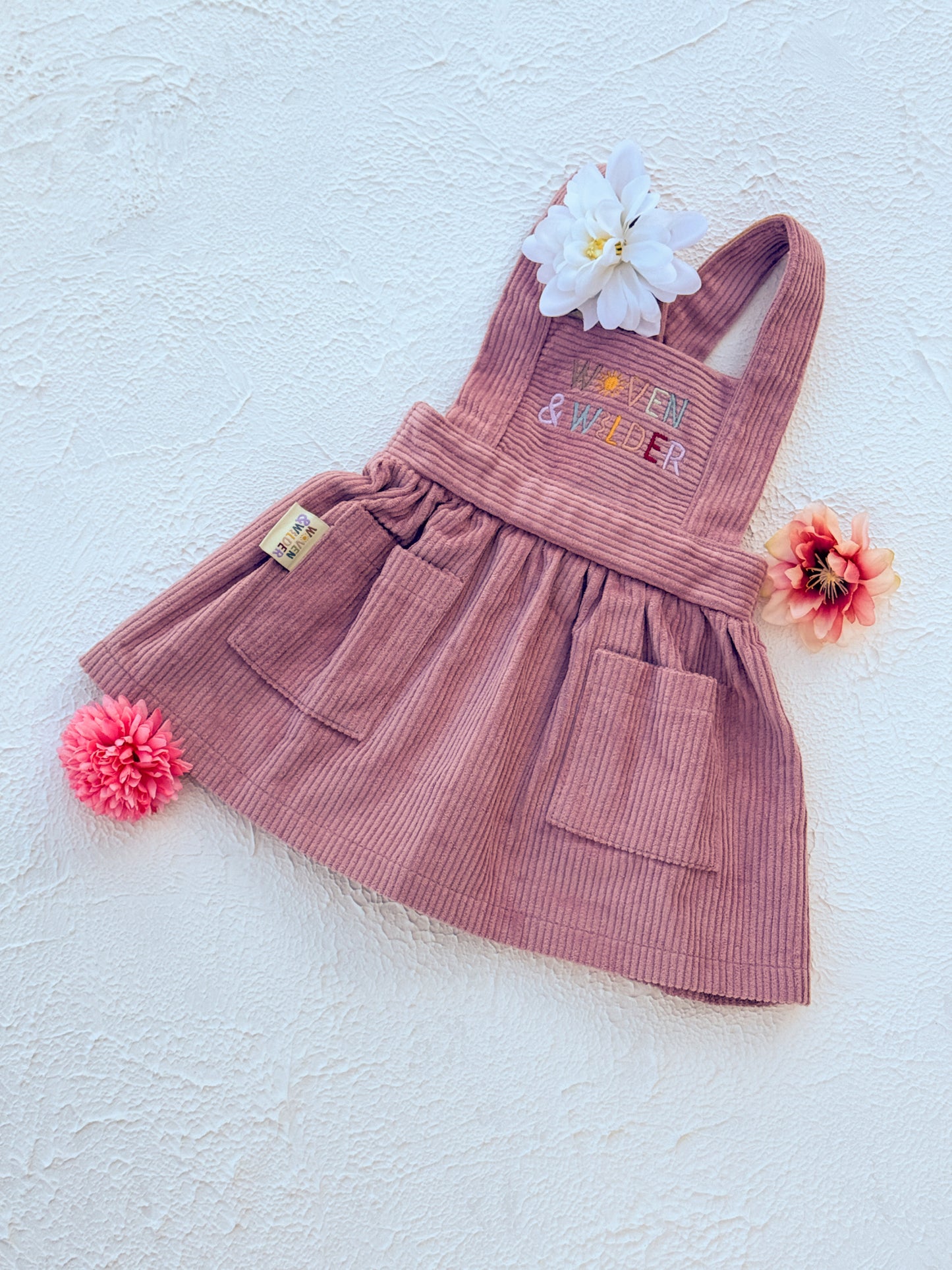 Pink dress with embroidered letters "Woven & Wilder" on a light blue background 