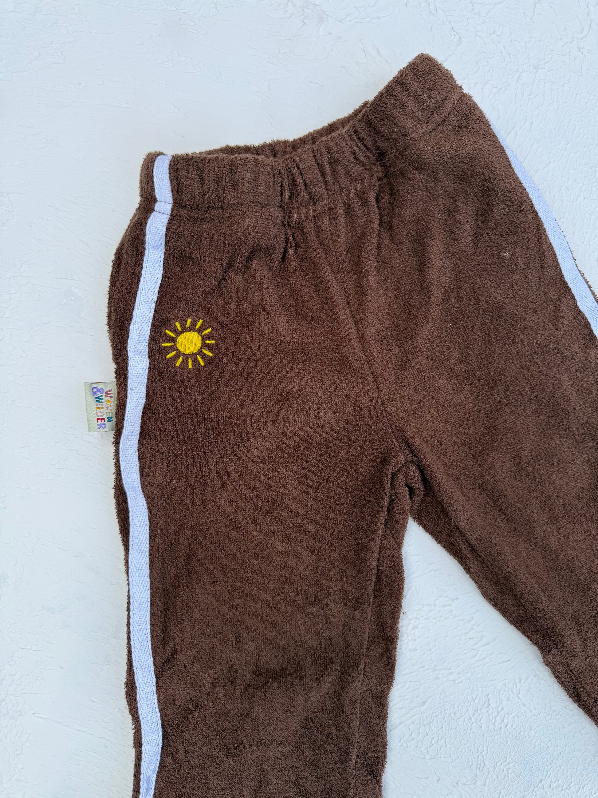 Brown sweatpants with a yellow sun logo on a light blue background