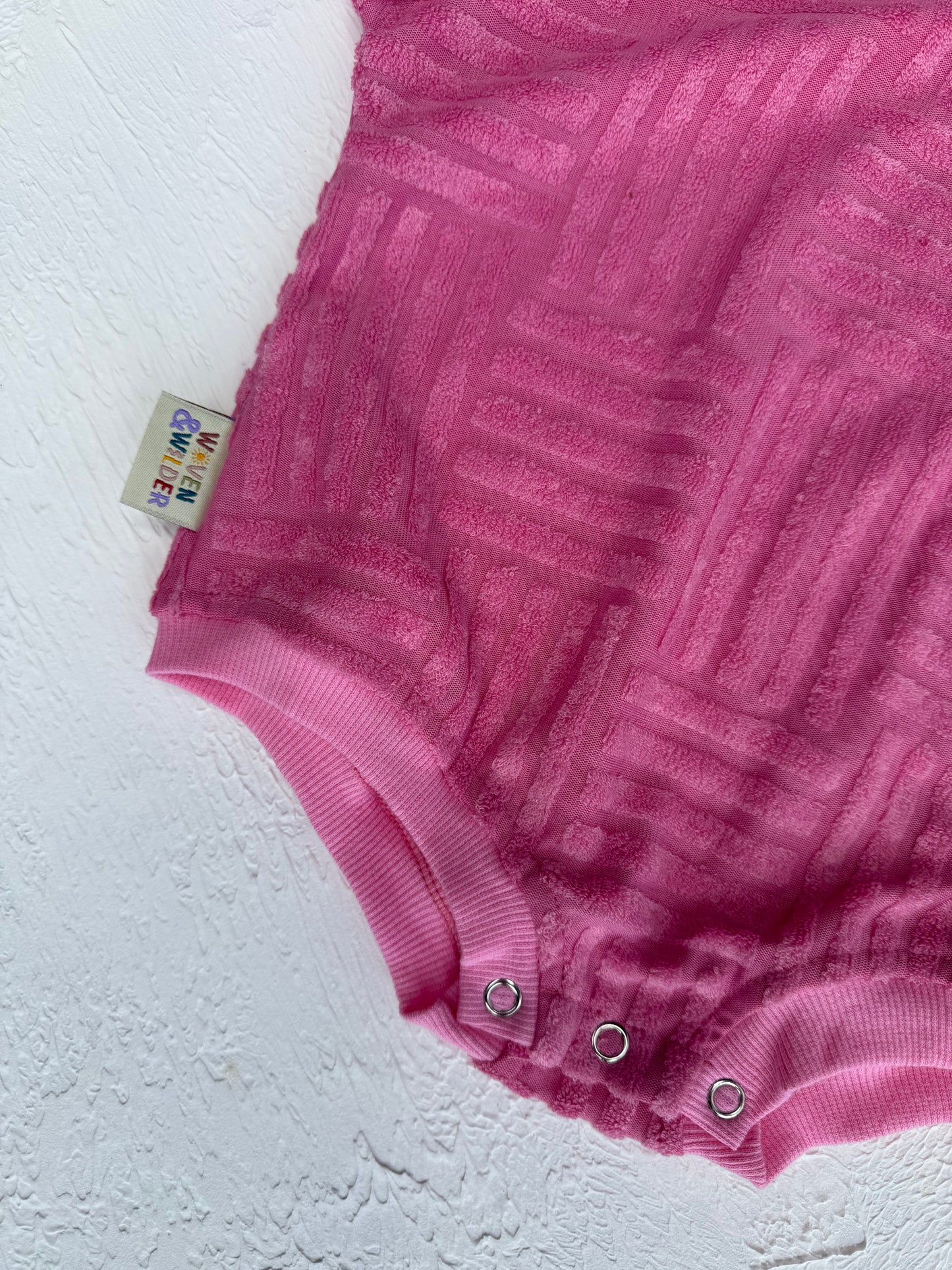 Pink baby romper with a brand tag on a white background