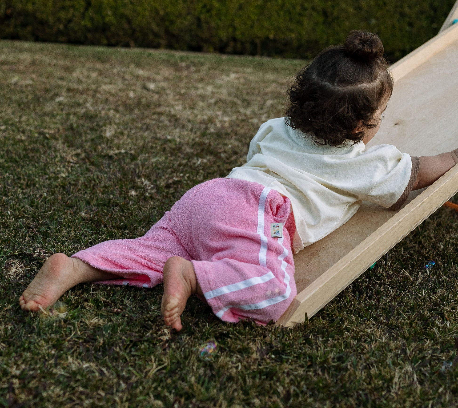 Child sliding down a small wooden slide on grass
