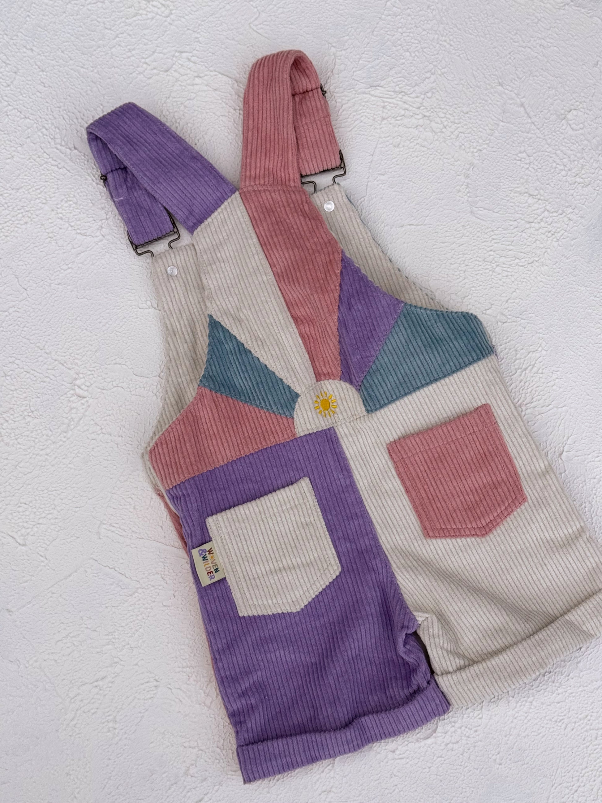 Color-blocked overalls with purple, green, and beige sections on a textured white background