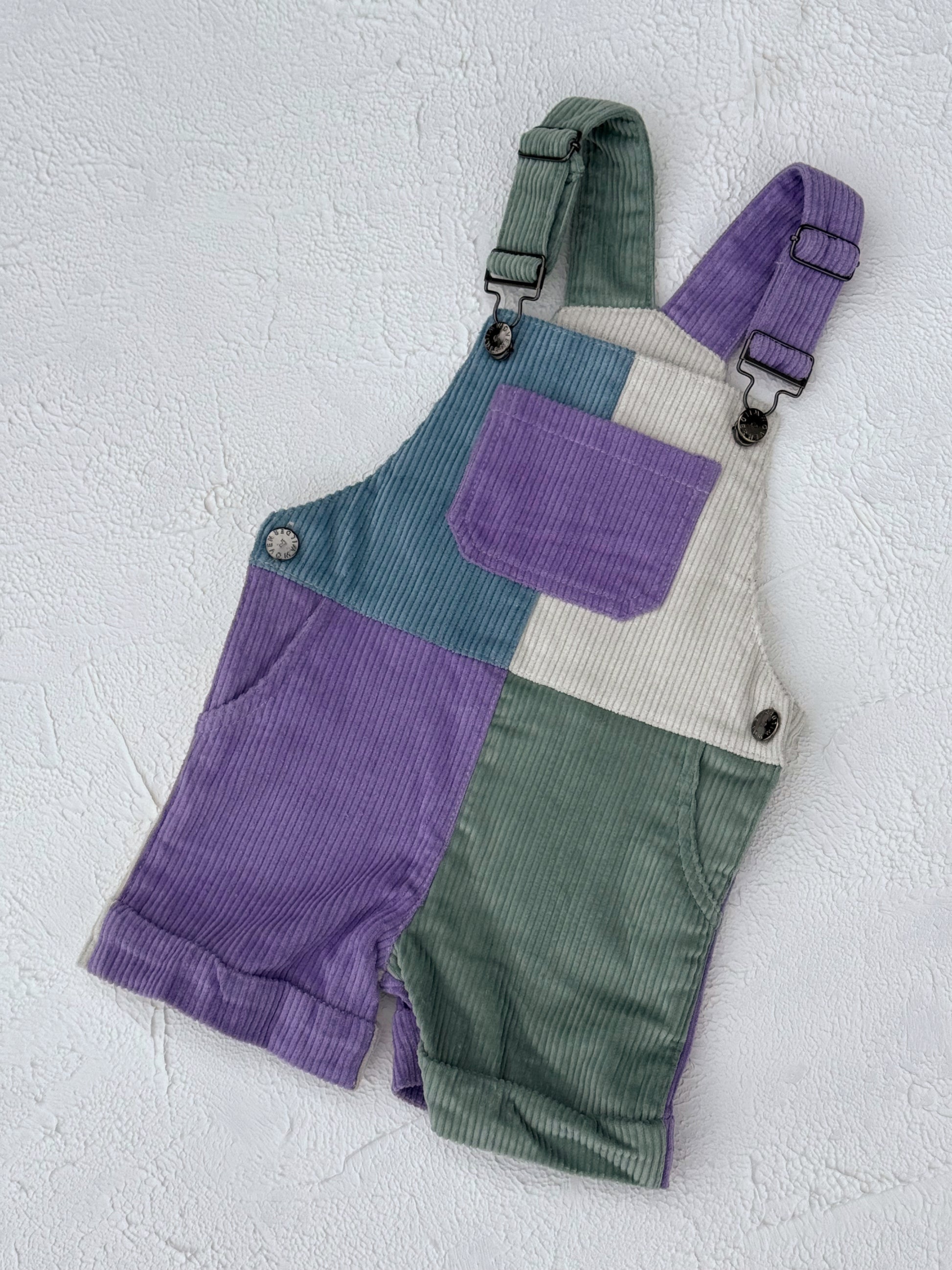 Color-blocked overalls with purple, green, and beige sections on a textured white background