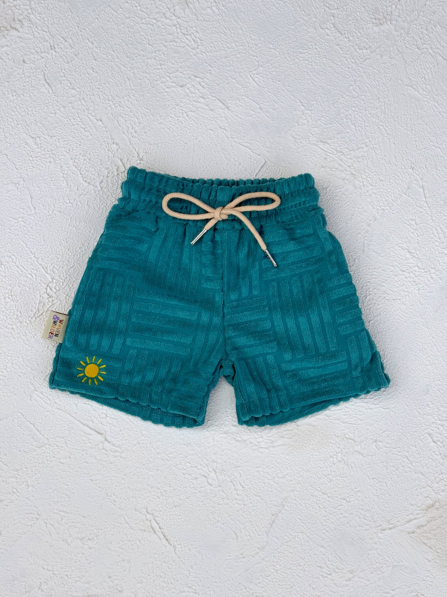 Teal shorts with a sun design on a textured white background