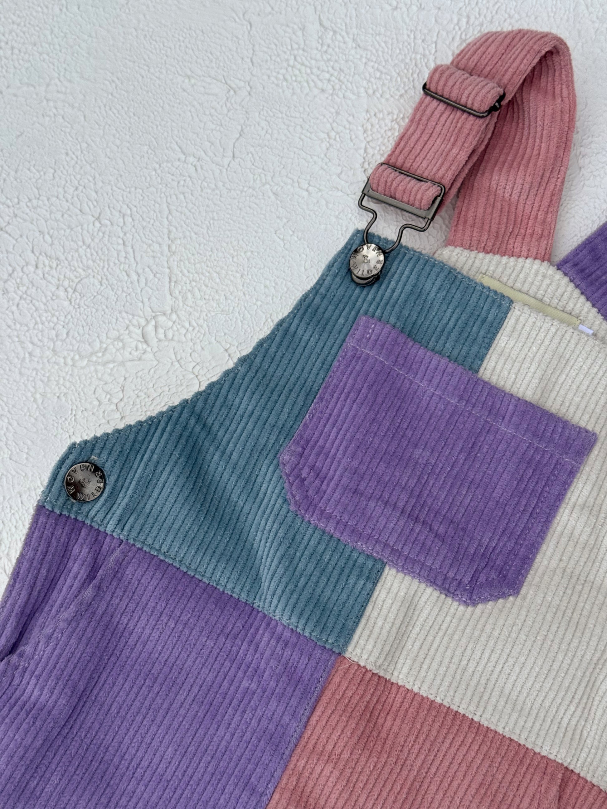Color-blocked overalls with purple, green, and beige sections on a textured white background