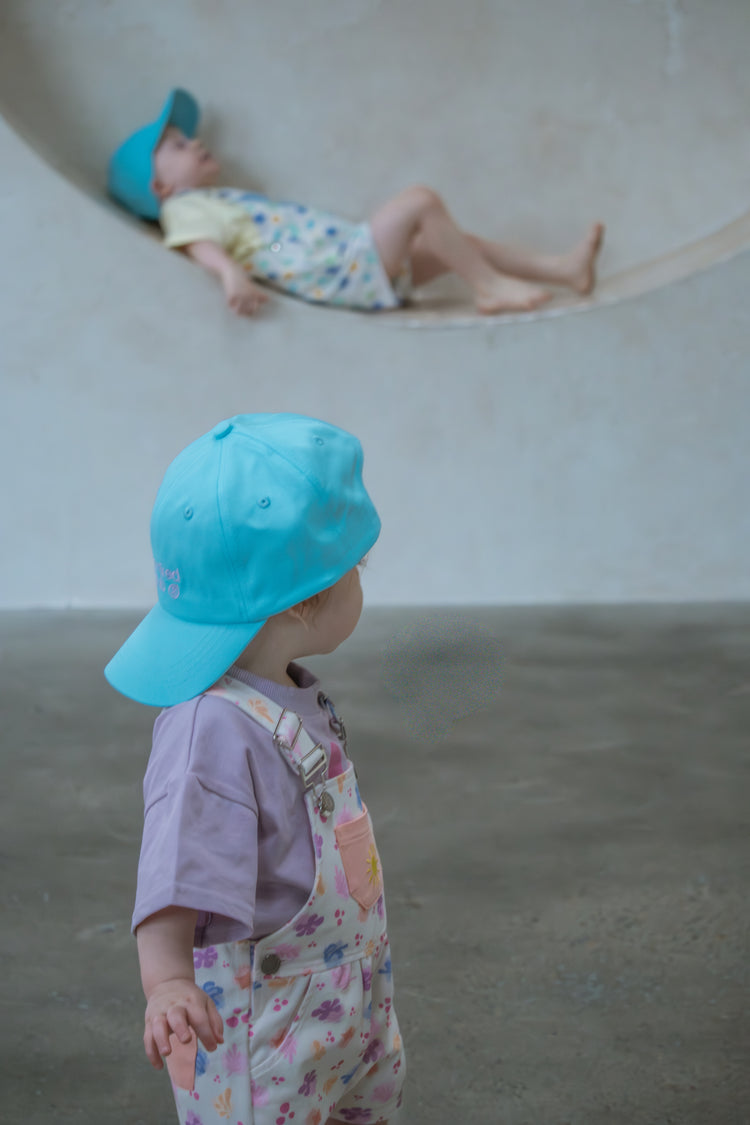 Two children wearing blue hats in a minimal indoor setting.