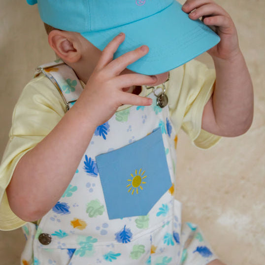 Child wearing a blue cap with text and a colorful outfit with a sun design.