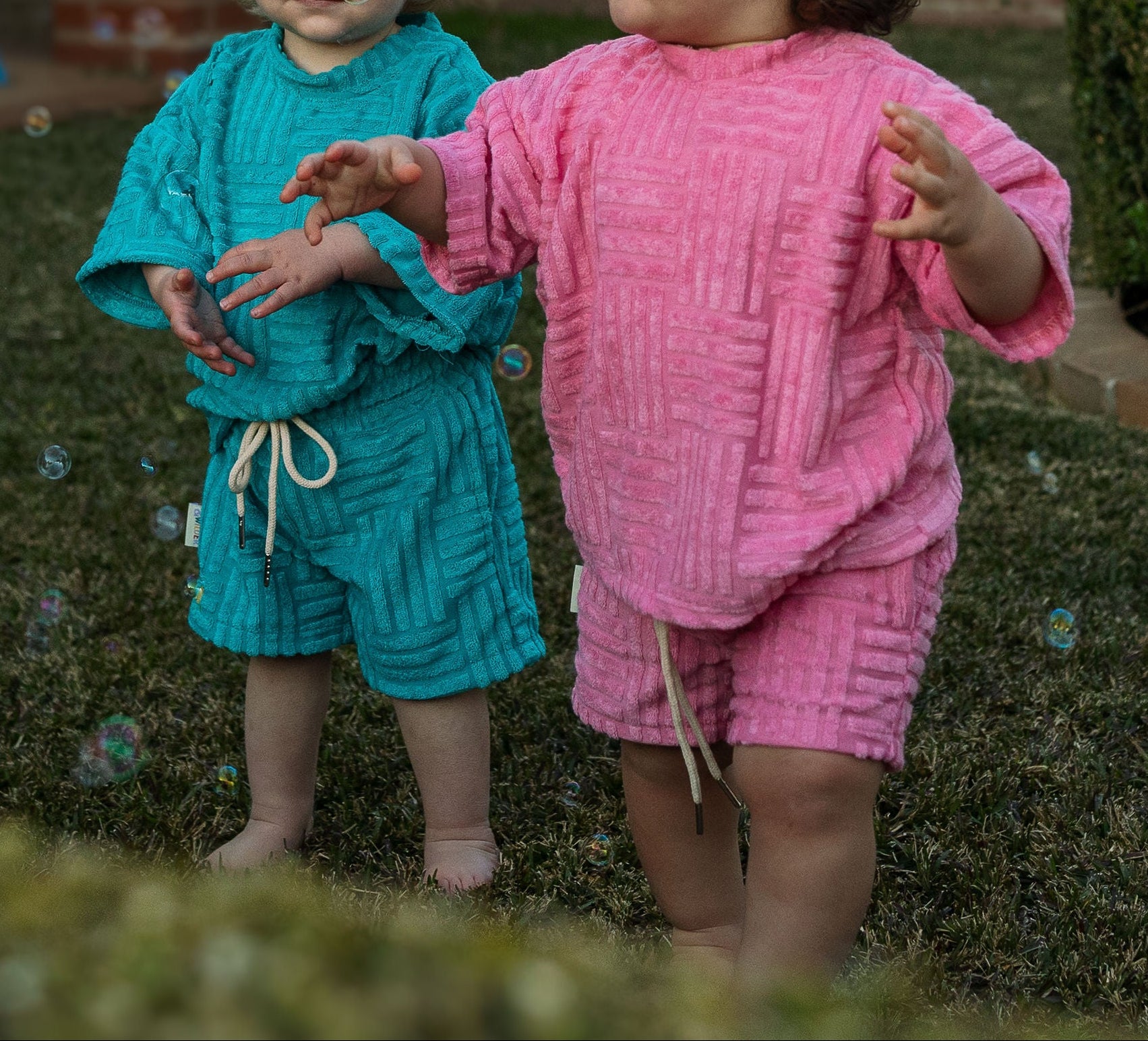 Two children in colorful knitted outfits standing on grass.