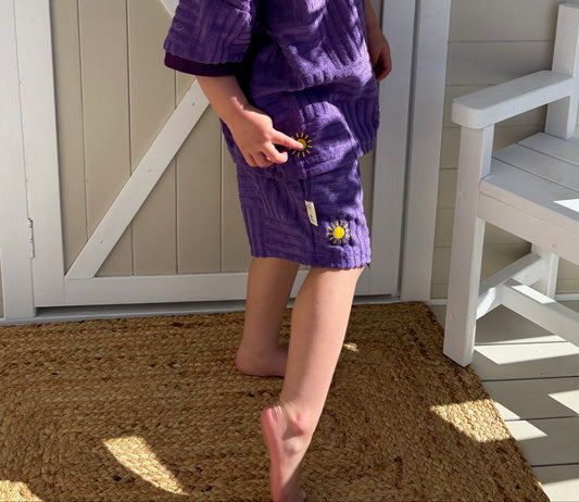 Child in a purple outfit standing in front of a wooden shed with 'Oaklee's Cubby' sign.