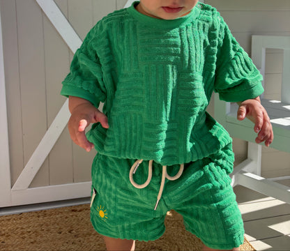 Child wearing a green outfit standing in front of a white wooden structure.